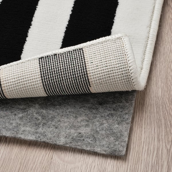 Black and white striped rug on light wooden floor, showing its backed side with a grey felt pad attached for grip and cushion.