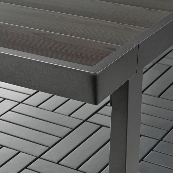 Close-up of VÄRMANSÖ outdoor table showing sleek, dark wood top and powder-coated metal frame, highlighting quality materials.