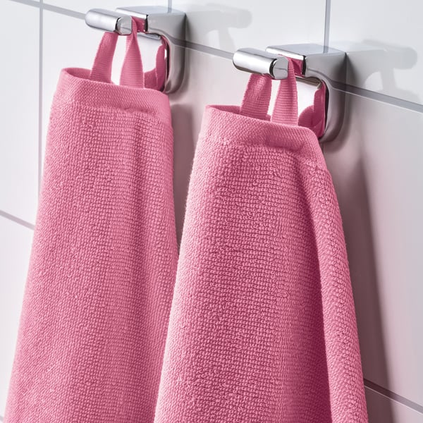 Two pink terry towels hang neatly on wall-mounted hooks, showcasing their absorbent, soft texture and quick-drying rib weave.