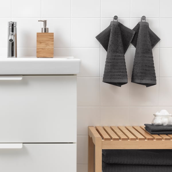 Modern bathroom with white sink, chrome tap, dark grey VÅGSJÖN towels, wooden soap dispenser, and slatted shelf.