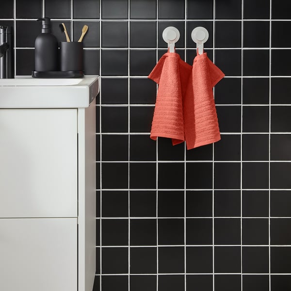 Bright orange VÅGSJÖN towel hangs on black grid tiles, near sink with toiletries.