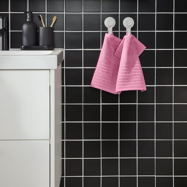 Modern bathroom with black tiles, pink VÅGSJÖN towels, white sink, black accessories.