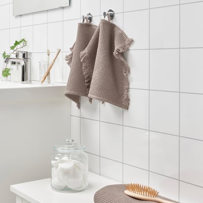 Bathroom with white tiles and two VALLASÅN towels. One folded with cotton rounds, brush beside. Absorbent, quick-drying waffle towels.