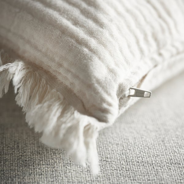 Close-up of soft, white cushion with raw edge fringe and hidden zip, showcasing quality and detail.