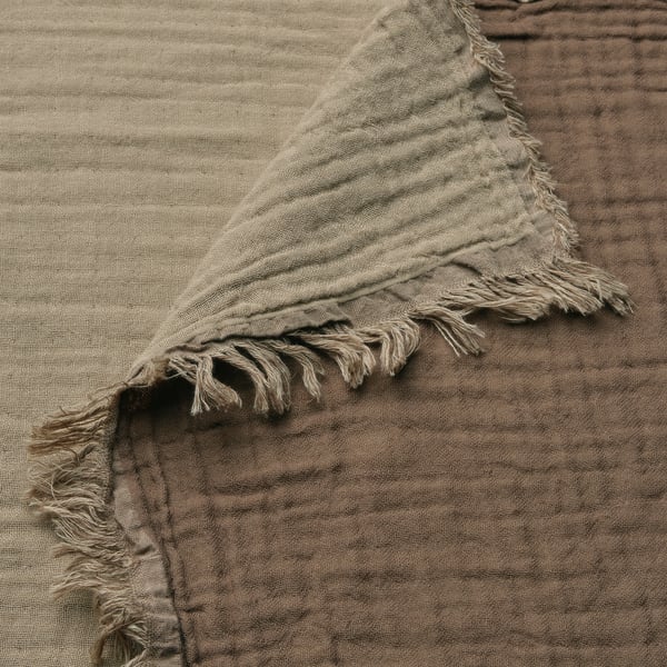 A close-up of a soft, textured beige throw blanket with crinkled fabric and frayed edges on a wooden surface.