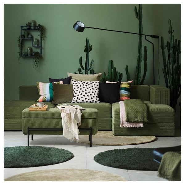 Green living room with green sofa, colourful pillows, cacti wallpaper, and floor lamp.