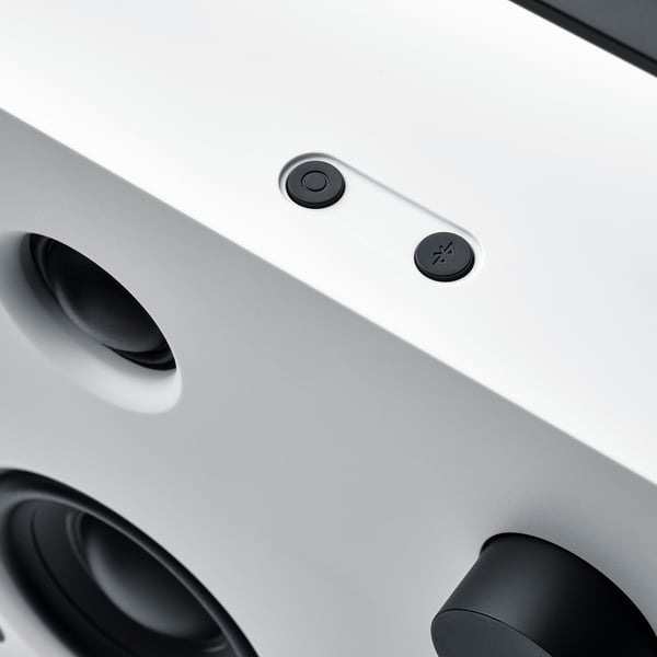 Close-up of sleek, modern white bluetooth speaker with smooth controls and dark accents.