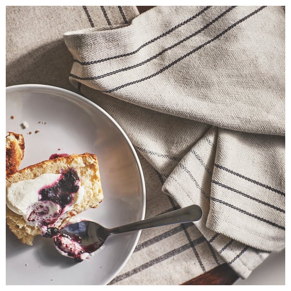 A dessert dish with whipped cream and blueberry sauce on striped linen.