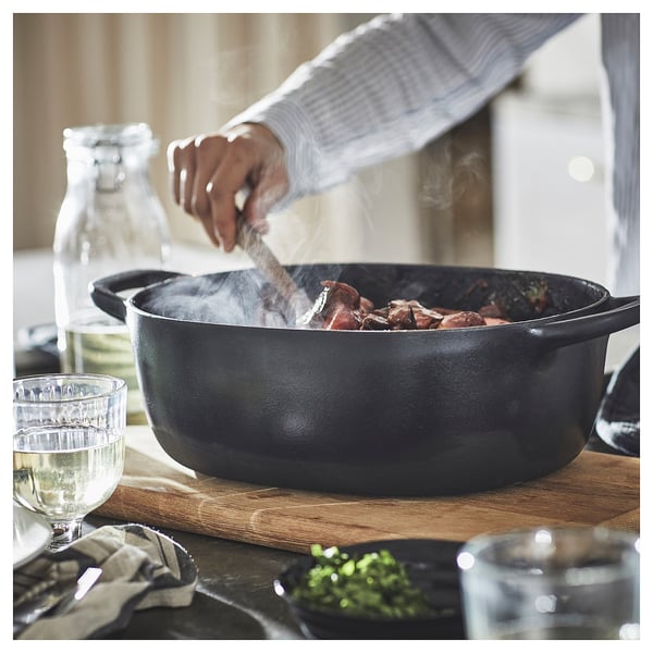 A person stirs food in a black cast iron pan on a wooden board, with glass cups around.