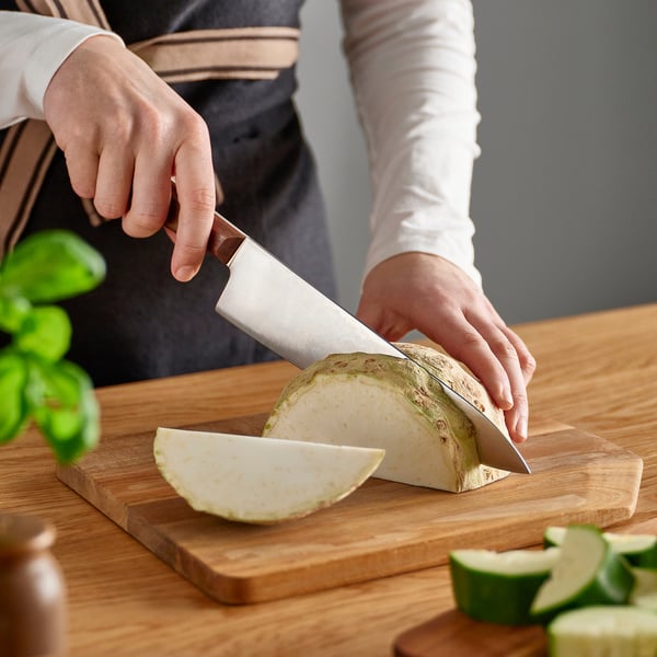 Person chopping vegetable on wooden cutting board using sharp, well-balanced knife.