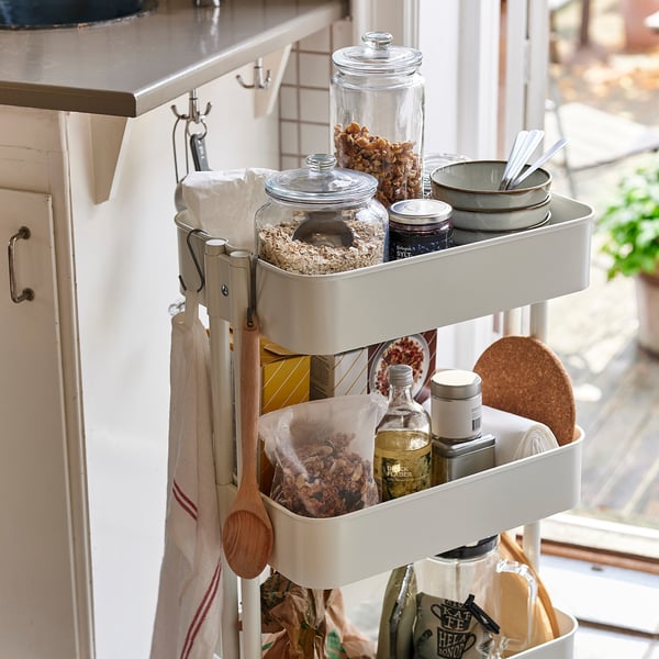 Kitchen cart with glass jars storing food, bowls, and utensils, positioned near a window for easy access and display.