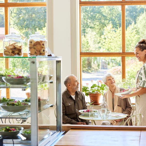 Elderly couple in cafe, salads in foreground, person smiling at waitress.