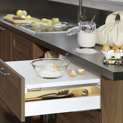 Kitchen counter with VARDAGEN bowl of sugar, apples, boards, toy car, and open drawer of spatulas.