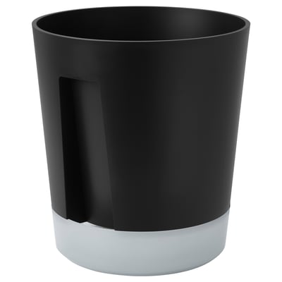 A black VÅRDTRÄD self-watering planter with a frosted white base, cylindrical in shape. It a handle and a side watering hole.