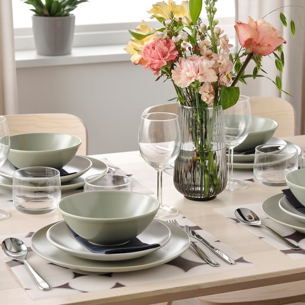 Table set with green dishes, glasses, cutlery, place mats, and a vase with flowers.