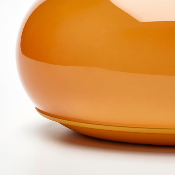 Sleek, orange glass lamp with smooth finish, casting warm glow. Modern, minimalist design, likely table or wall mount.