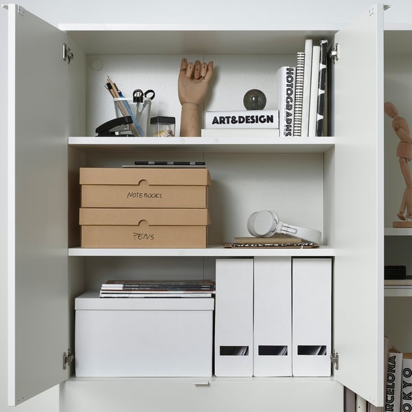 White cabinet with art, design books, and VATTENTRÅG boxes for notes and pens, organised neatly.