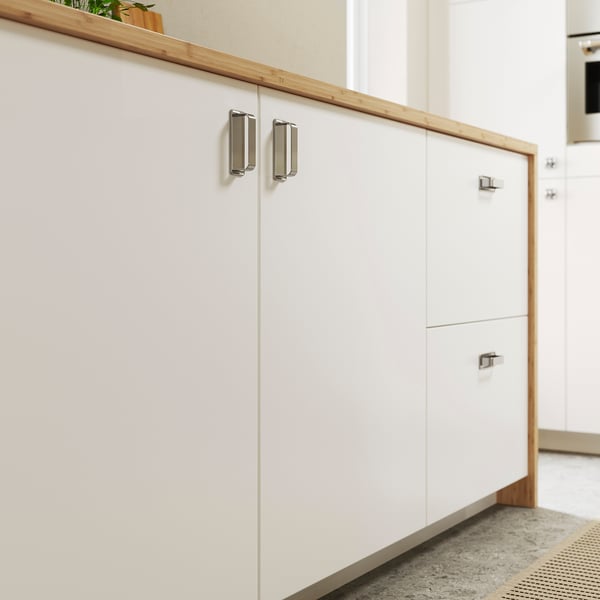 White modern kitchen cabinets with silver handles. Smooth, clean lines. Top shelf with potted plant. Light, spacious feel.