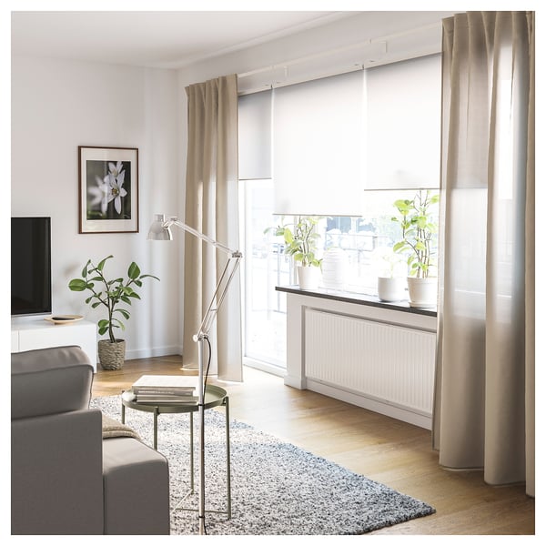 Modern living room with light-colored curtains, grey sofa, coffee table, and plants. Large window with VIDGA curtain rail system.