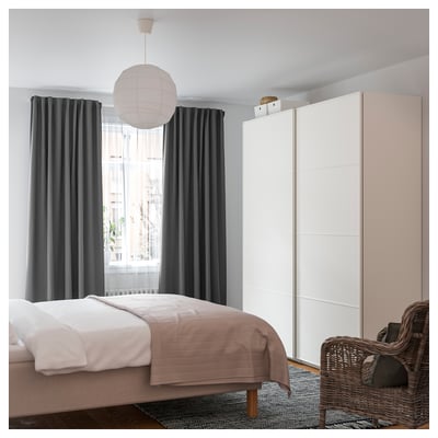 Bedroom with beige bed, large window, pendant light, wicker chair.