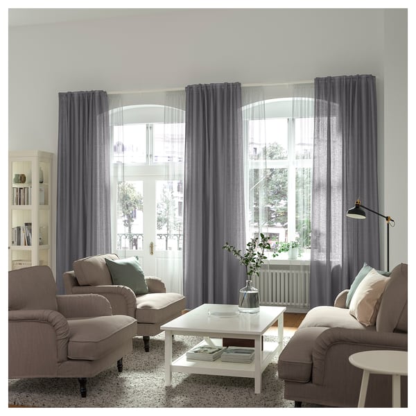 Living room with grey curtains, large window, two sofas, coffee table with white lamp.