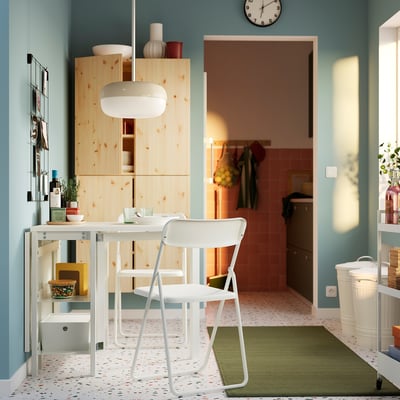 Modern kitchen with white wood cabinets and blue walls. White VIHALS folding chair against pine table. Bright, spacious, simple design.