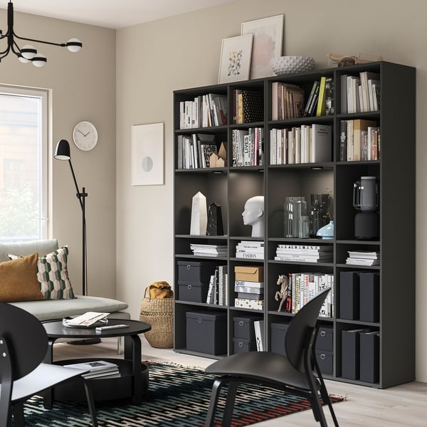 Modern black VIHALS storage unit, tall with multiple shelves, holding books and decor, beside a window and couch.