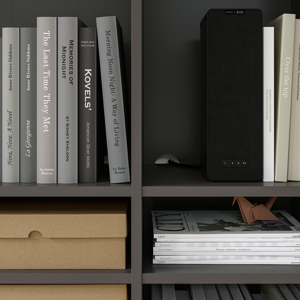 Bookshelf with black speaker, books, paper folder, magazines, and storage boxes. Neatly organised, high-quality design.