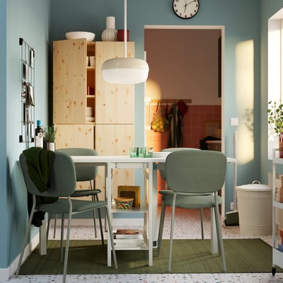 Modern dining space with white VIHALS table and green chairs. Light wood cabinets, blue walls, and a room divider visible in the background.