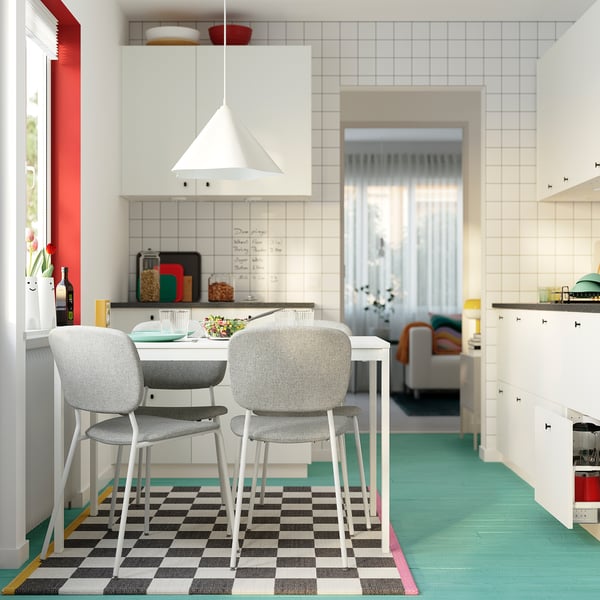 Modern kitchen with white VIHALS table, grey chairs, chequered rug, green floor, white cabinets, and hanging lamp.