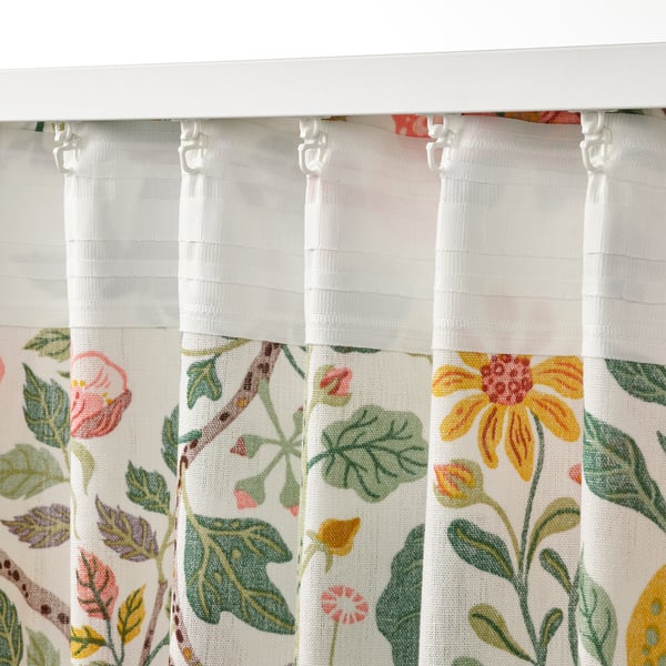 A pair of white curtains, adorned with colourful floral patterns, hung neatly with visible tabs and hooks for light filtering and privacy.