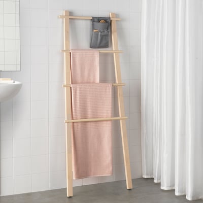 Wooden towel stand with pink towels and toiletries pouch in bathroom corner.