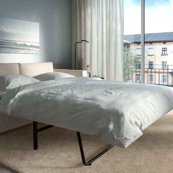 Modern bedroom with large window, sofa-bed featuring thick mattress, and city view.