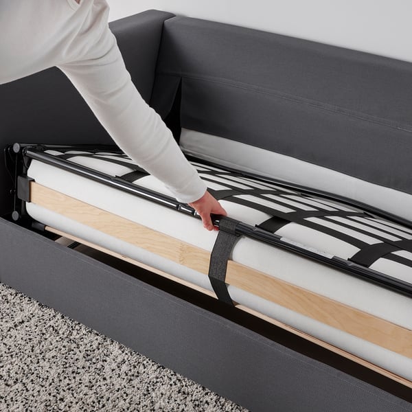 Person adjusts convertible sofa-bed with thick mattress, showcasing its easy transformation and comfort.
