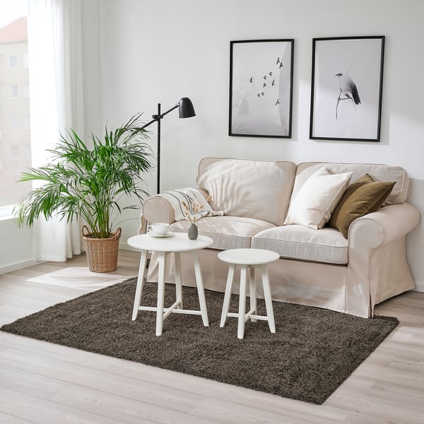 Cosy living room with VINDEBÄK rug, two-tone grey, soft, plush, under light sofa, two side tables, tall plant.