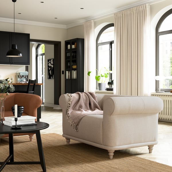 Modern living room with beige VISKAFORS armchair, wooden coffee table, black curtains, and large arched windows.