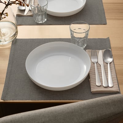Two places set with VITBLECKA white tempered glass plates, grey napkins, silverware, and glasses; minimalist, elegant design.