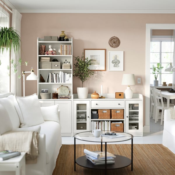Bright living room with VITTSJÖ coffee table. White couch, glass-top table, bookshelf with decor. Natural light, potted plants.