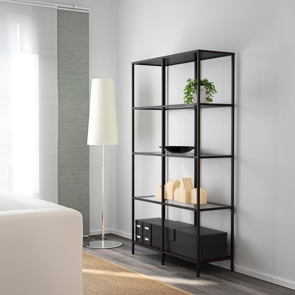 Modern bookshelf with glass shelves against a wall, holding decorative objects and a plant.