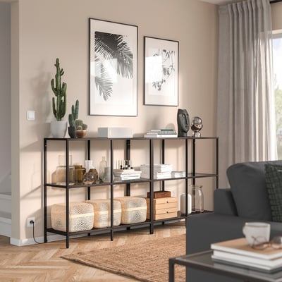 Modern living room with VITTSJÖ black shelf, plants, vases, and books. Sofa partially visible, tidy and stylish.