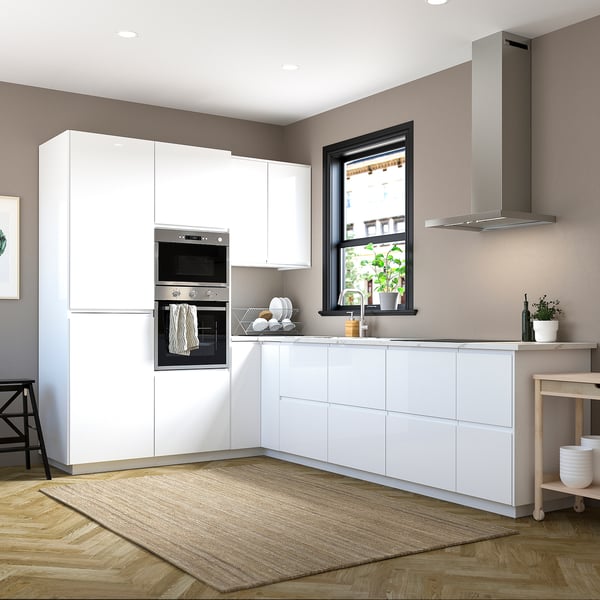 Modern kitchen with white high-gloss cabinets and integrated handles, stainless steel appliances, large window, wooden floor, and beige rug.