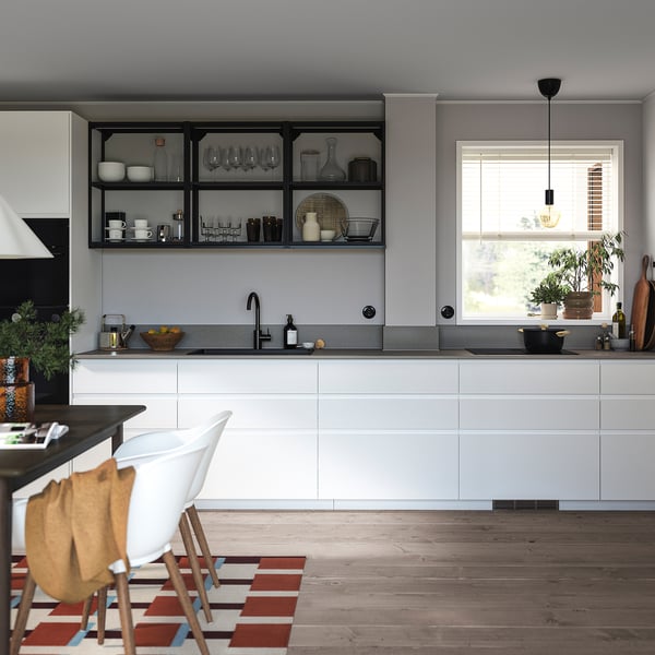 Modern kitchen with white cabinets, black fixtures, wood floors, open shelves with cookware, and a dining area with white chairs.
