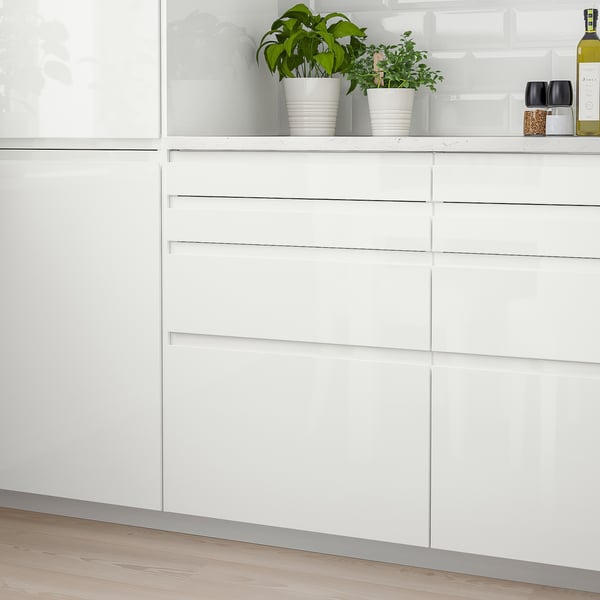 White glossy kitchen cabinet with sleek integrated handles, smaller than potted plants on top.
