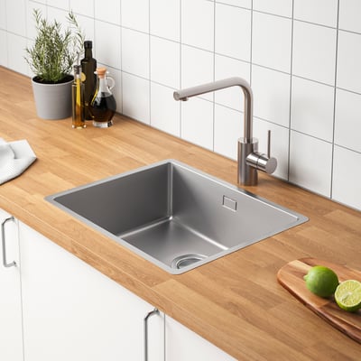 Modern kitchen sink with stainless steel tap, wooden countertop, and bottles, limes, and plant decor.