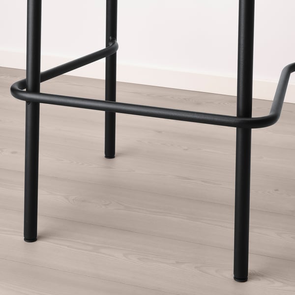 Black metal bar stool with curved back support, sturdy legs, on wooden floor.