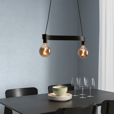 ACKJA lampa ar divām spuldzēm virs tumša galda komplekta ar traukiem.