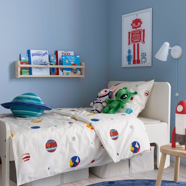 Bērnu istaba ar AFTONSPARV segu, planētām, zvaigznēm, zilu sienu, grāmatu plauktu, sarkanu robotu plakātu, zilo planētu spilvenu, zaļu rotaļlietu, sarkanu raķešu lampu.