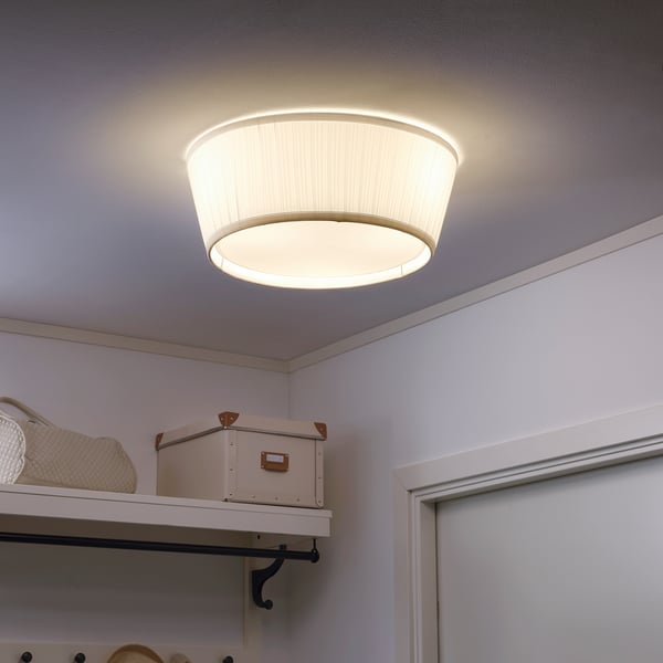 Griestu lampa nodrošina mīkstu, izkliedētu gaismu, kas ideāli piemērots telpām; uzstādīts uz baltiem griestiem ar uzglabāšanas plauktiem zemāk.