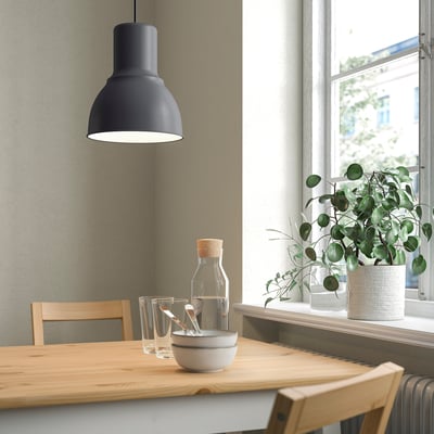 Mūsdienīga ēdamistaba ar melnu piekaramo lampu virs koka galda, ko ieskauj zaļi augi.