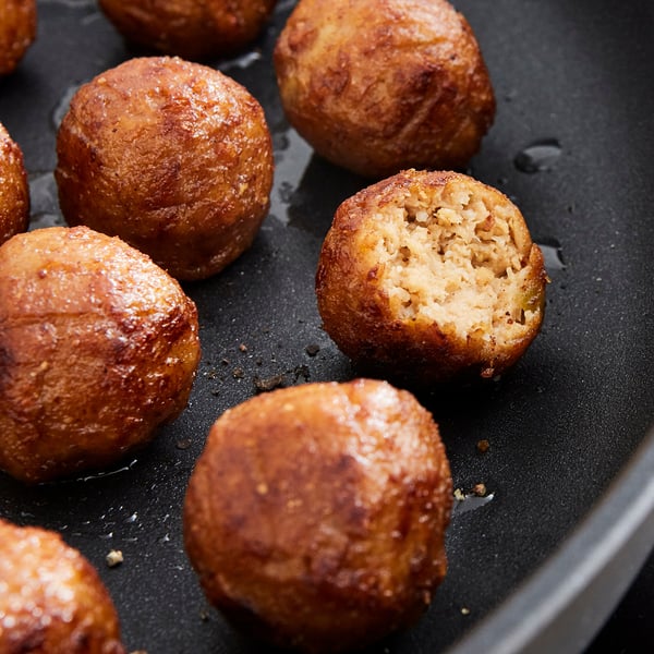 Zeltaini brūnu, apaļu, kraukšķīgu fritteru raksti sizzling melnā pannā. Viens ir sagriezts, atklājot mīkstu, gaļai līdzīgu interjeru.